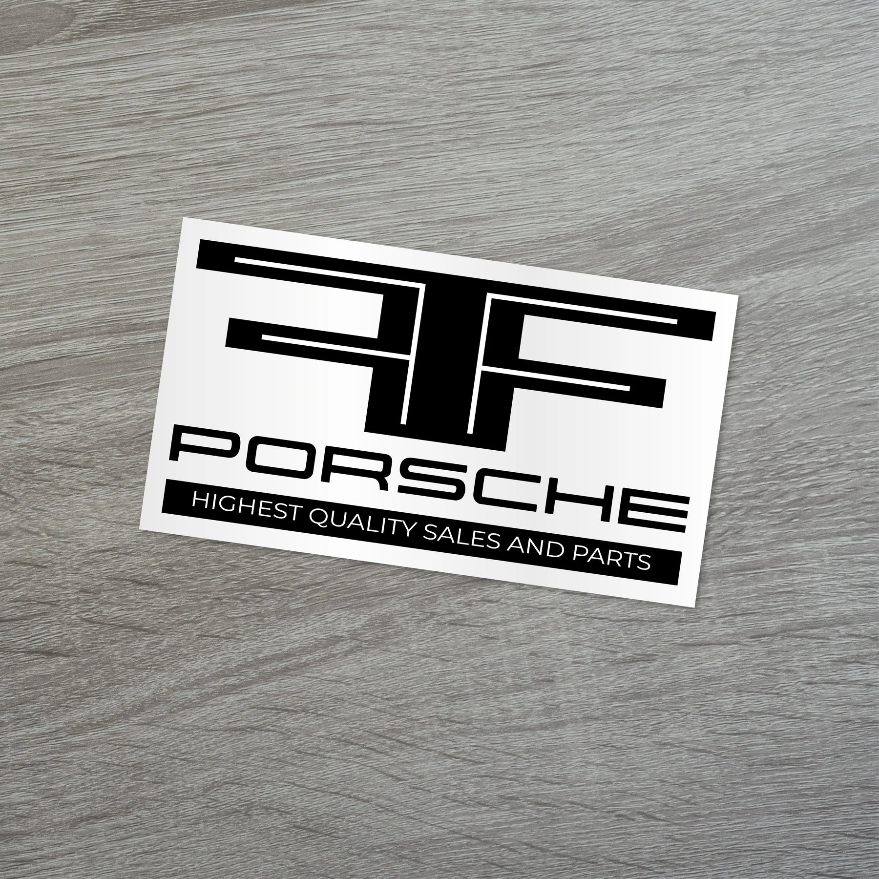 Porsche car dealership sticker showcasing highest quality sales and parts on a wooden surface.