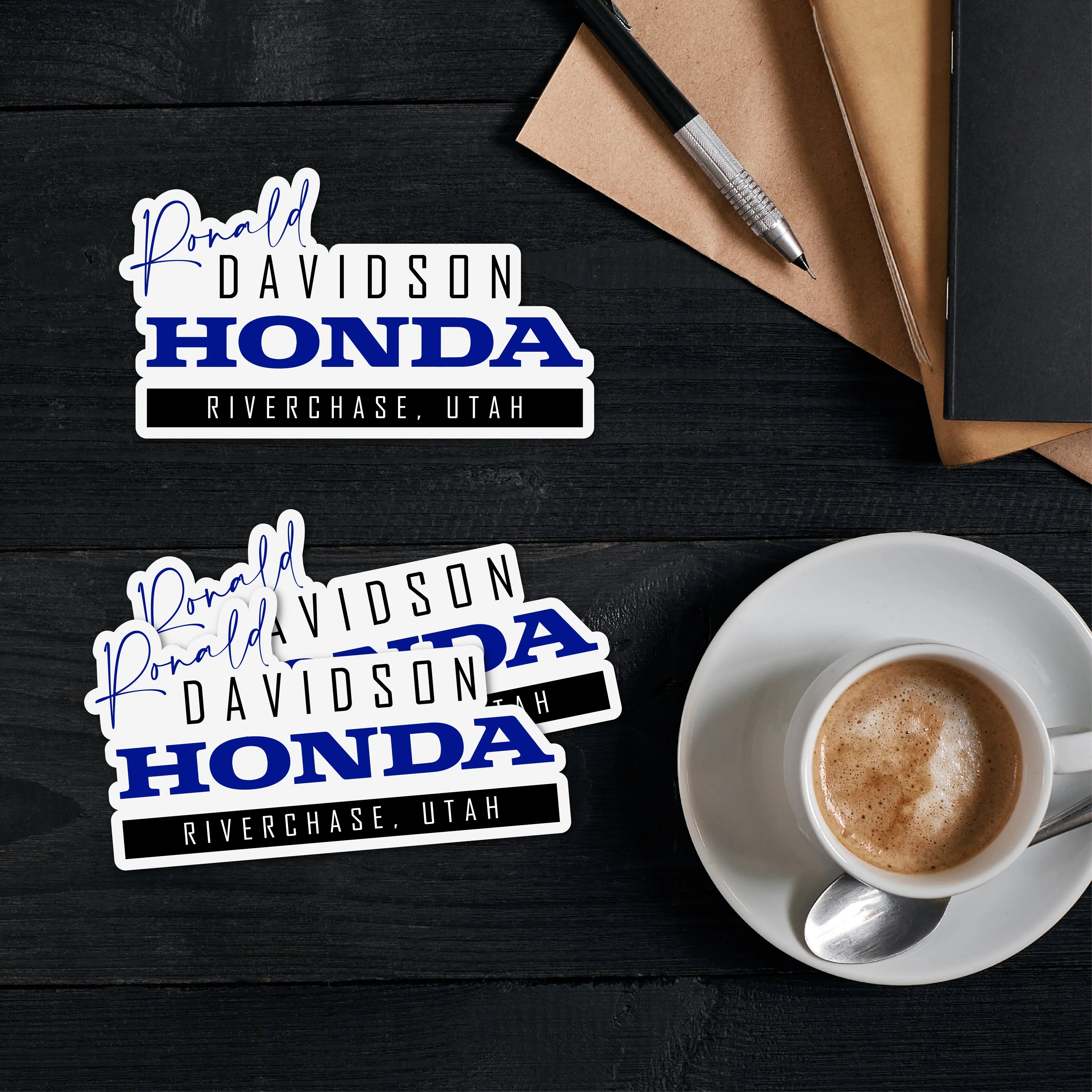 Custom car dealership stickers featuring Donald Davidson Honda, Riverchase, Utah on a desk with coffee.