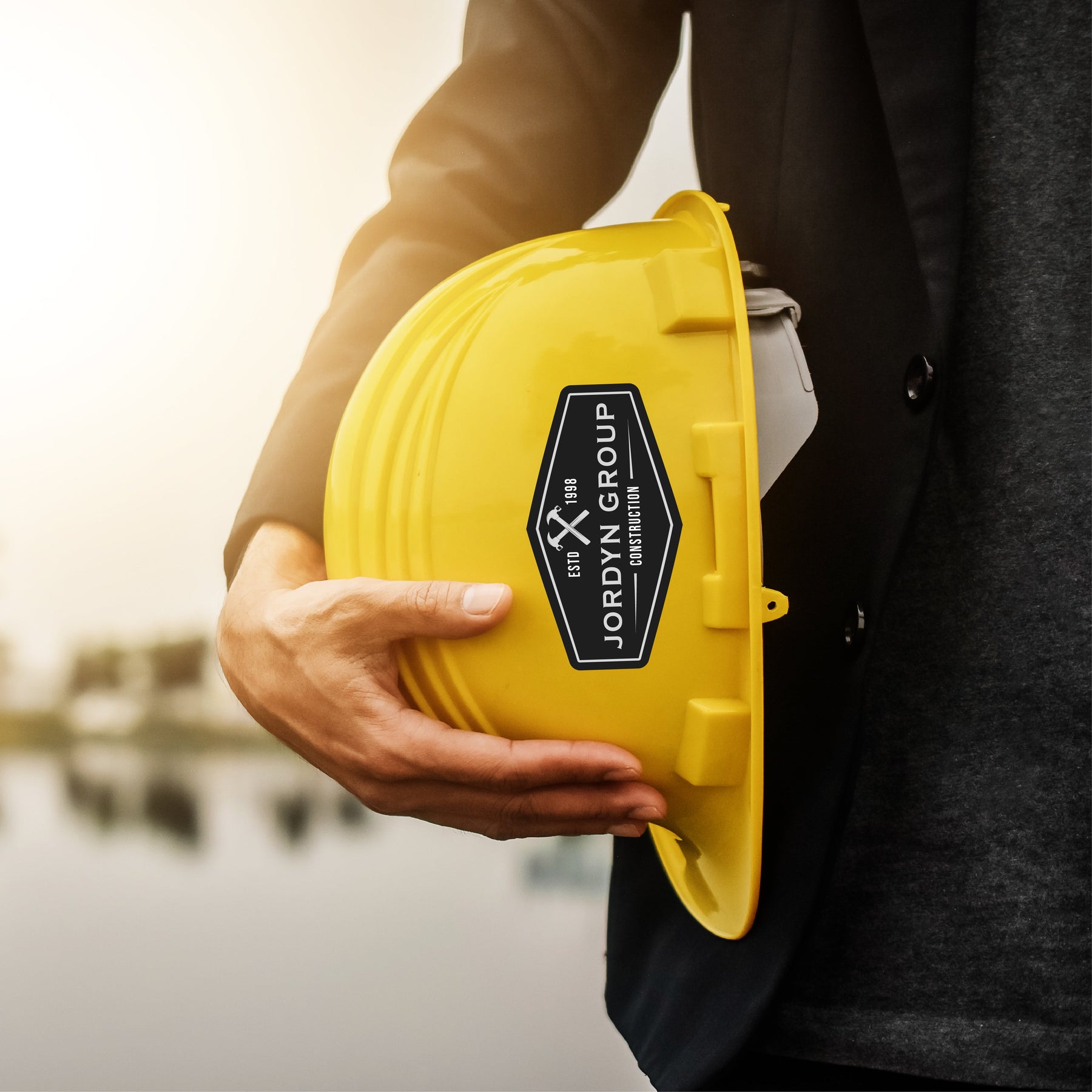 Person holding a yellow hard hat featuring heavy duty stickers for durability in tough environments.